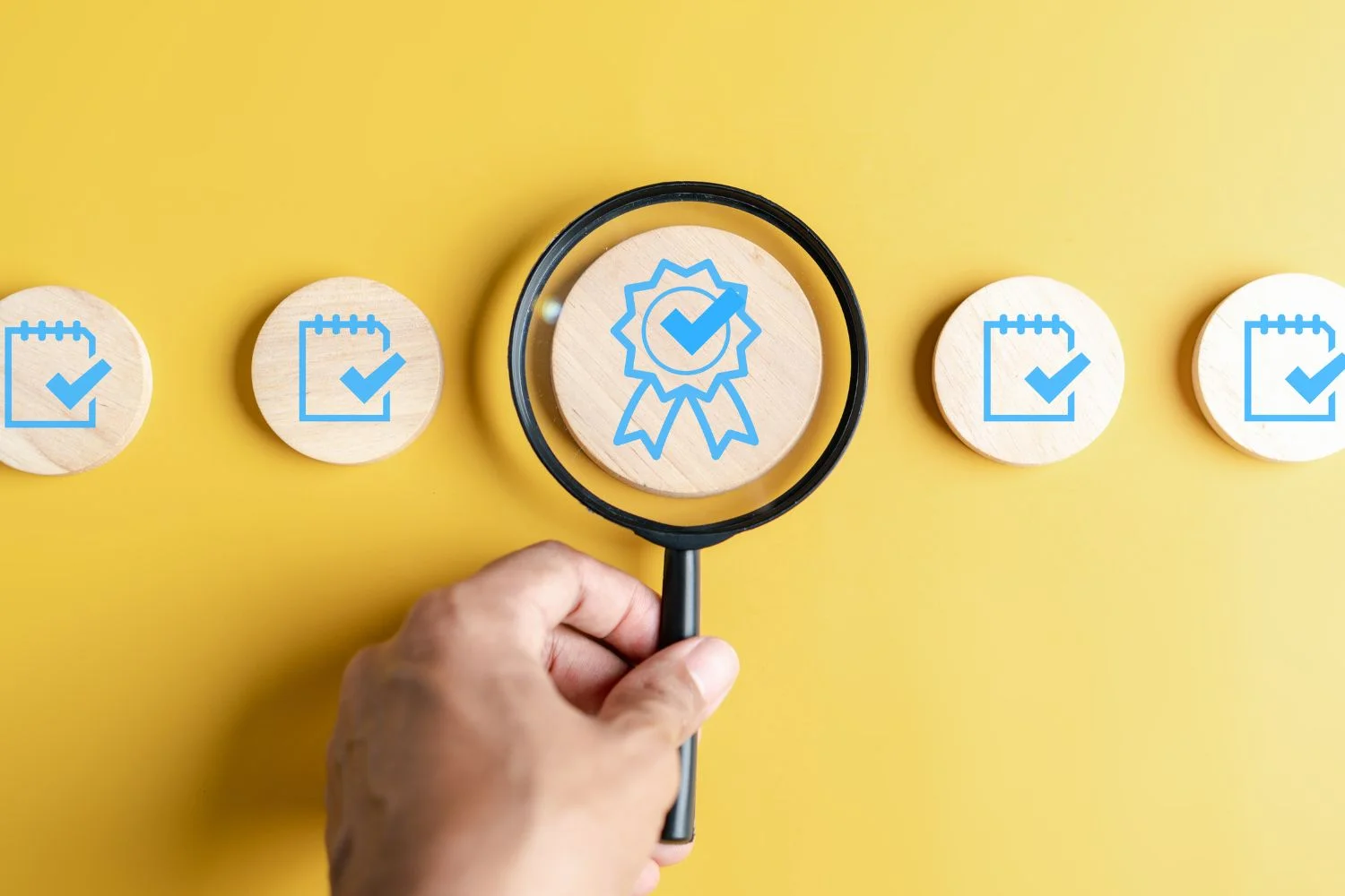 Image of a hand holding a magnifying glass evaluating icons representing credentials and a checklist