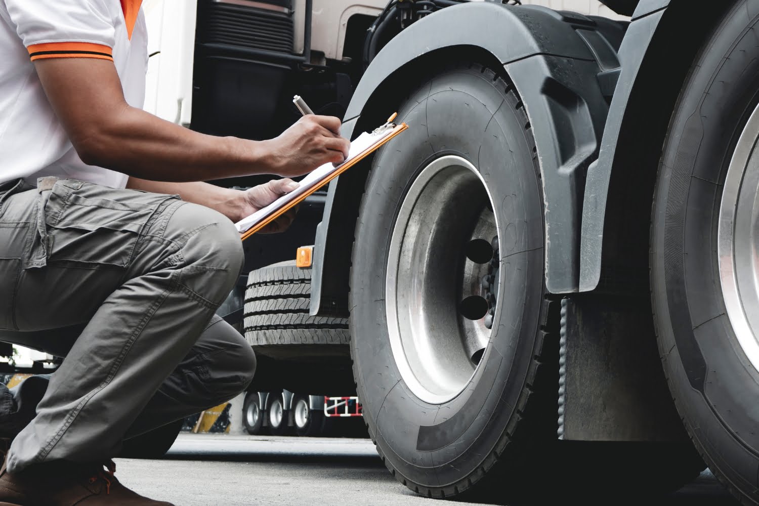 An image of a worker checking a freight truck's tires with a clipboard