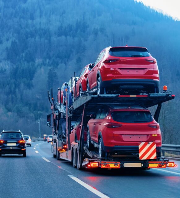 An image of a car transport truck driving on a roadway next to passenger vehicles